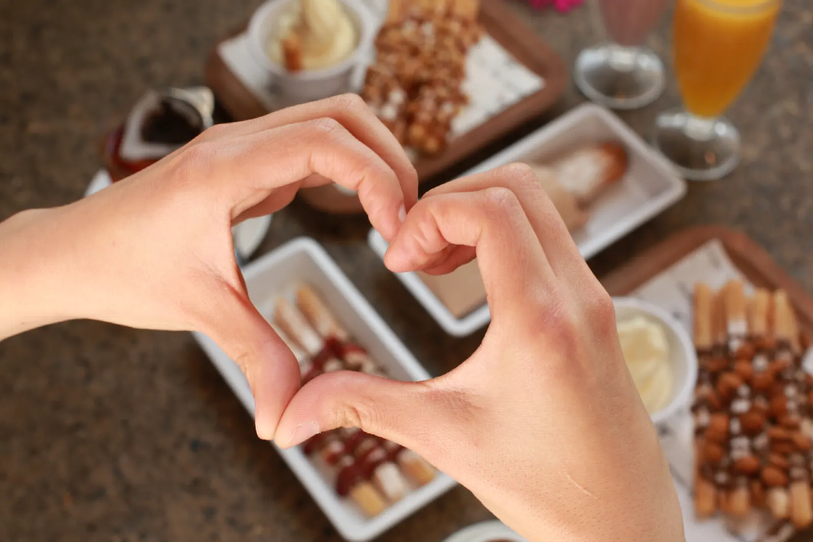 Manos formando un corazón sobre una mesa con churros y chocolate